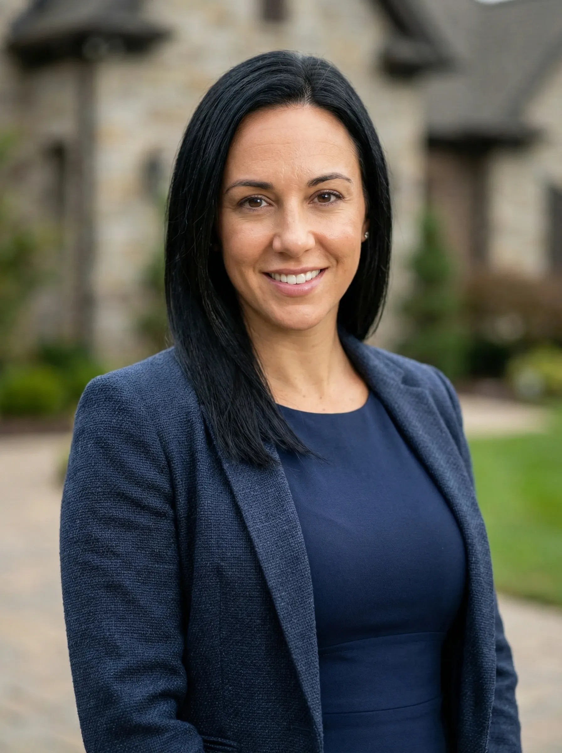 AI realtor headshot — woman in a navy blazer and navy dress outside a luxury home